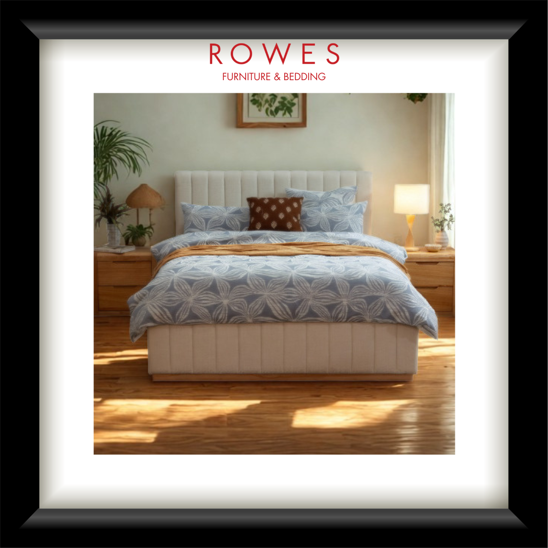 A bedroom scene featuring a large, plush bed with a fabric bedhead and foot, bedsides on a timber floor. The Rowes Furniture logo features.