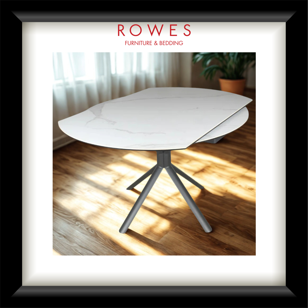 White dining table with gray legs on a wooden floor, branded as Rowes Furniture & Bedding.