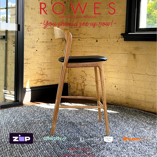 Wooden bar stool with black seat in a room with Brick walls and large windows.