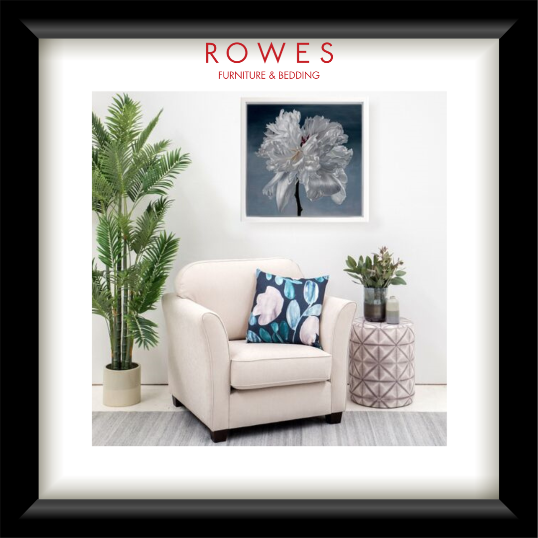 Furniture and bedding advertisement featuring a cream armchair with a floral pillow, potted plant, and side table.