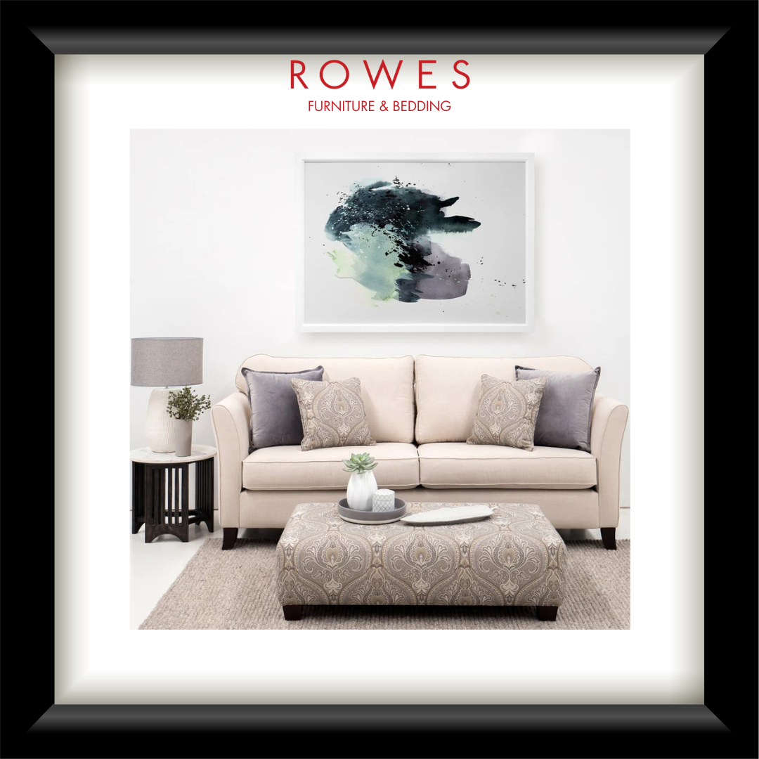 Living room with beige sofa, ottoman, and abstract art on a white wall, featuring 'Rowes Furniture & Bedding' logo.