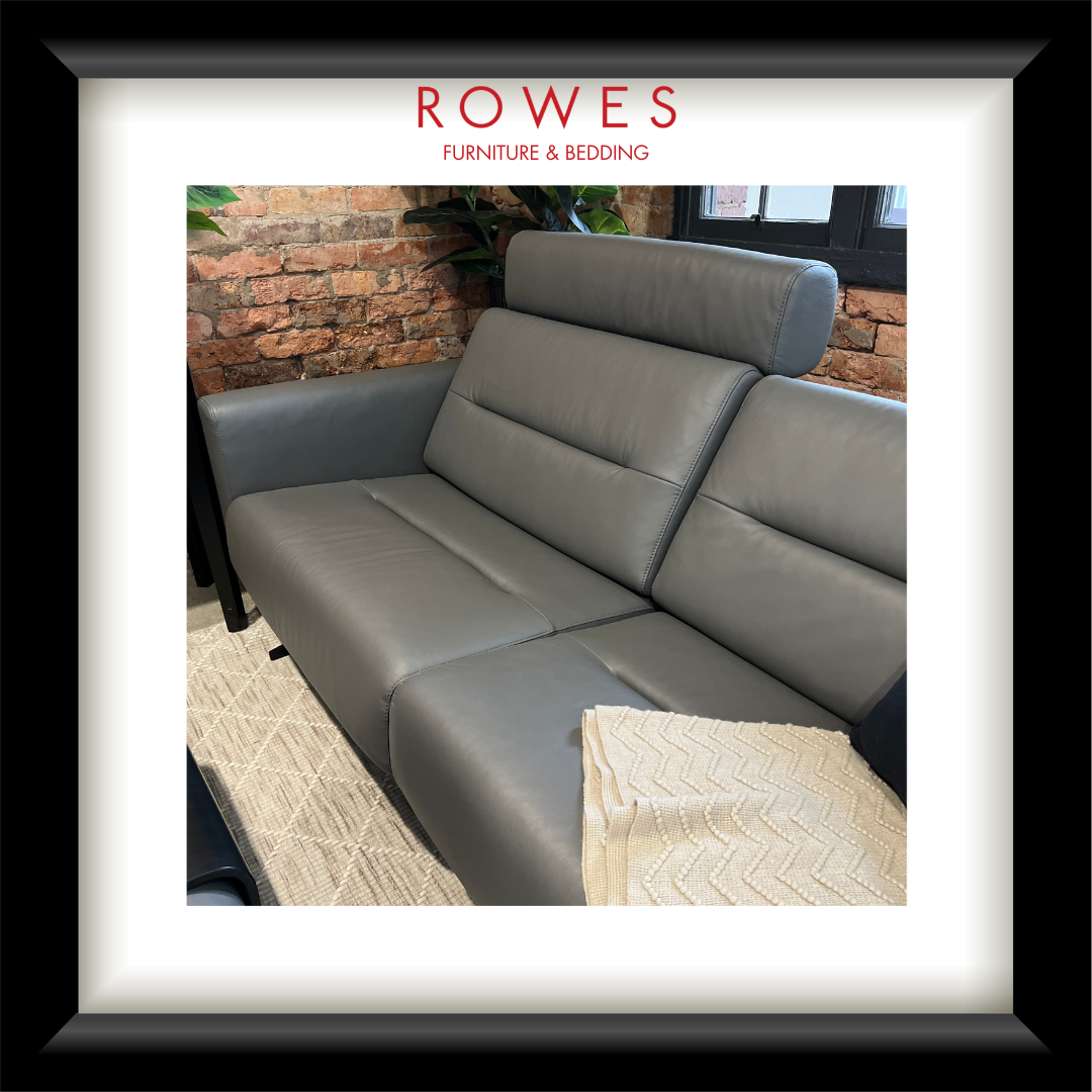 Gray sofa in a room with brick walls and a rug, branded with 'Rowes Furniture & Bedding'.