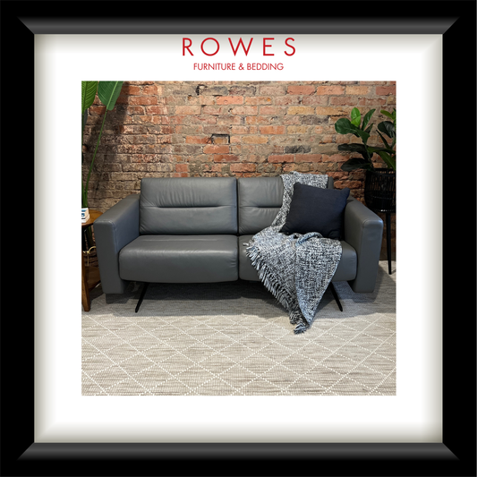 Gray sectional sofa with a blanket and pillow against a brick wall, featuring 'Rowes Furniture & Bedding' branding.