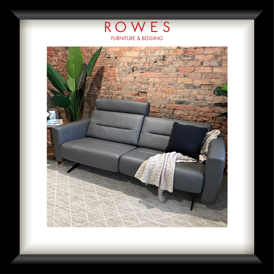 Gray sofa with a blanket and pillow against a brick wall, featuring 'Rowes Furniture & Bedding' logo.