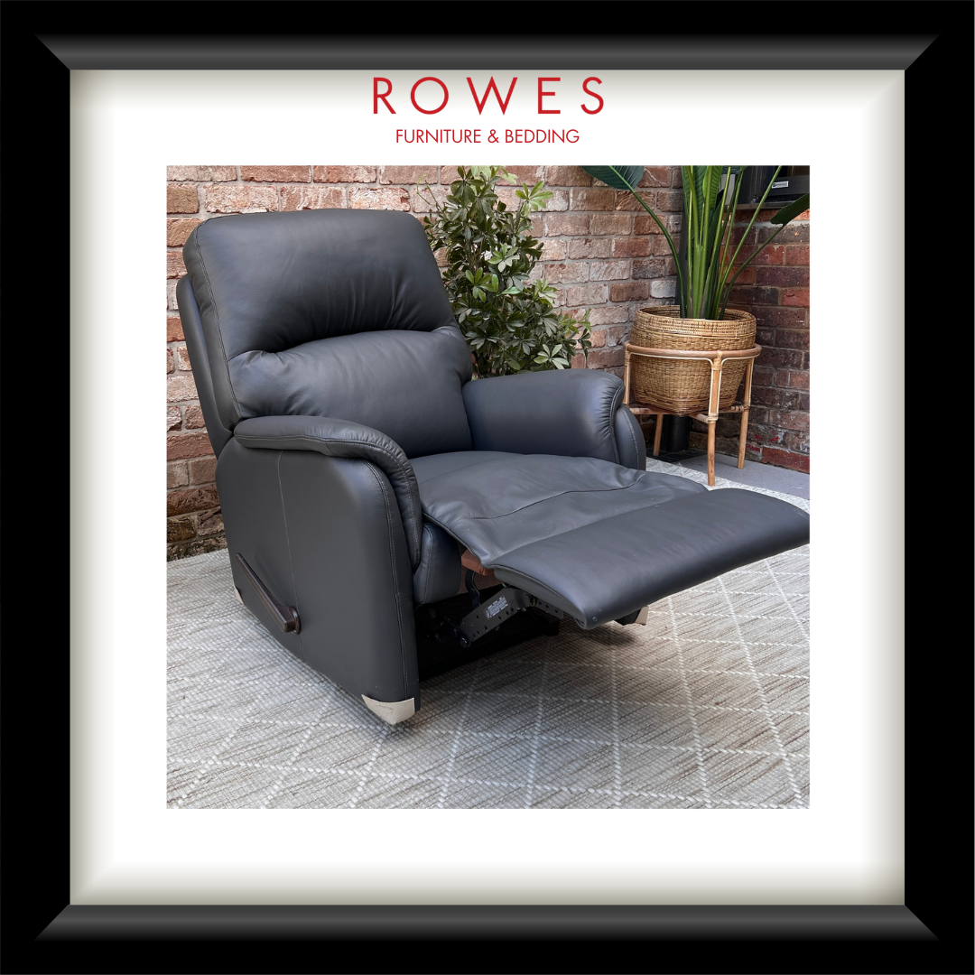 Gray recliner chair in a room with plants and a brick wall, branded as Rowes Furniture & Bedding.