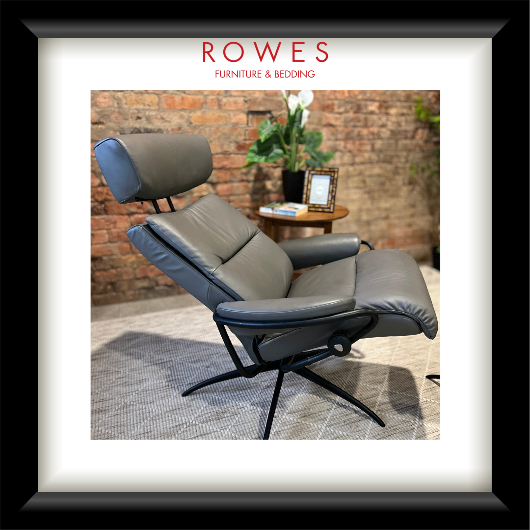 Gray recliner chair with headrest in a room with a brick wall and plants.
