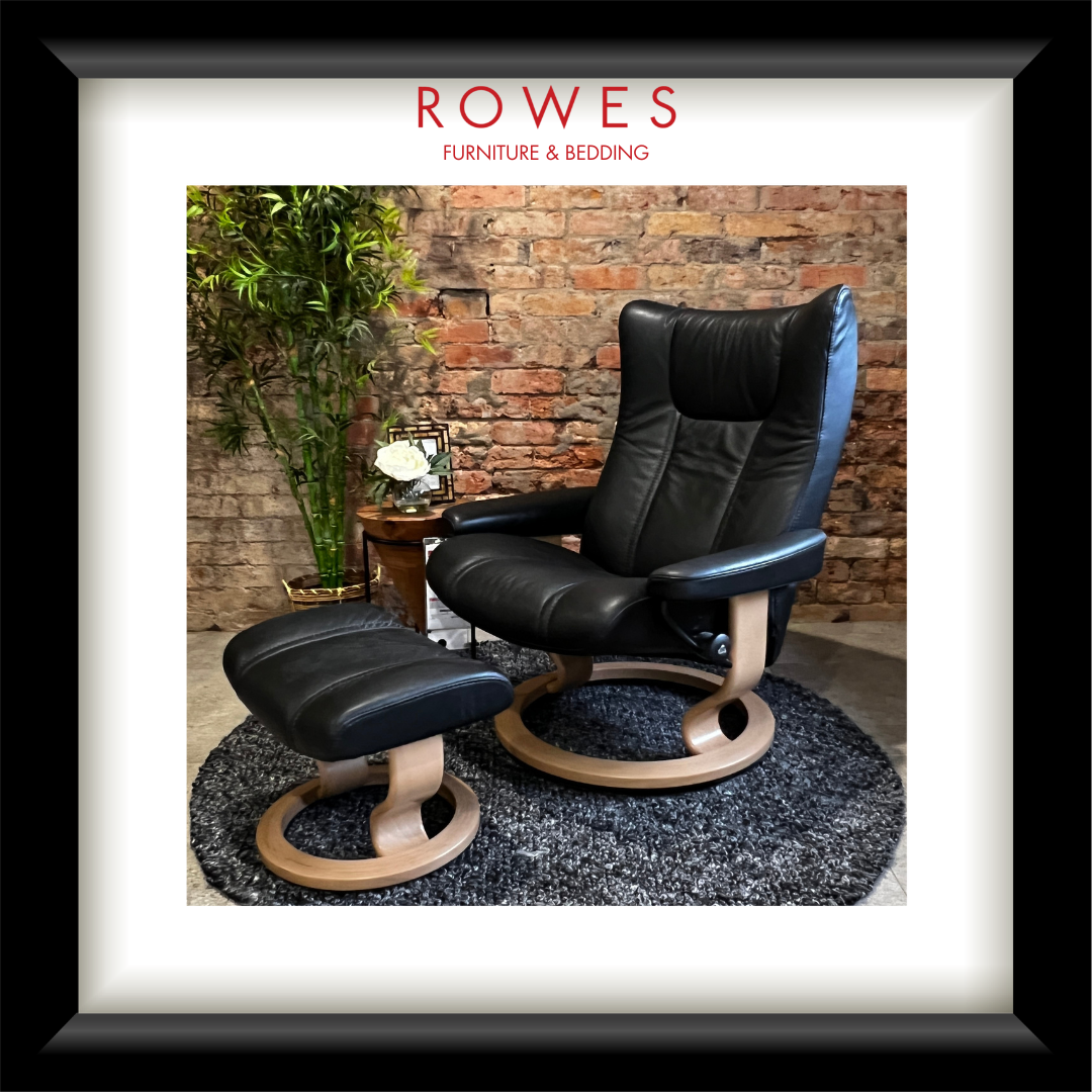 Black leather armchair and ottoman with wooden legs in a room with brick wall and plants, branded 'Rowes Furniture & Bedding'.