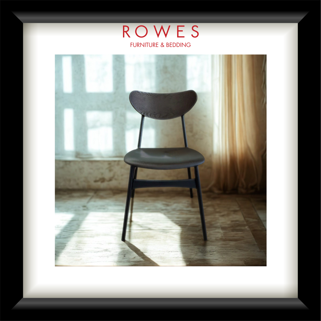 A framed interior photo print featuring a black wood dining chair with a black upholstered seat cushion in a sunlit room. The print has a white mat and a thick black frame, with the red text 'ROWES FURNITURE & BEDDOING' centered at the top.