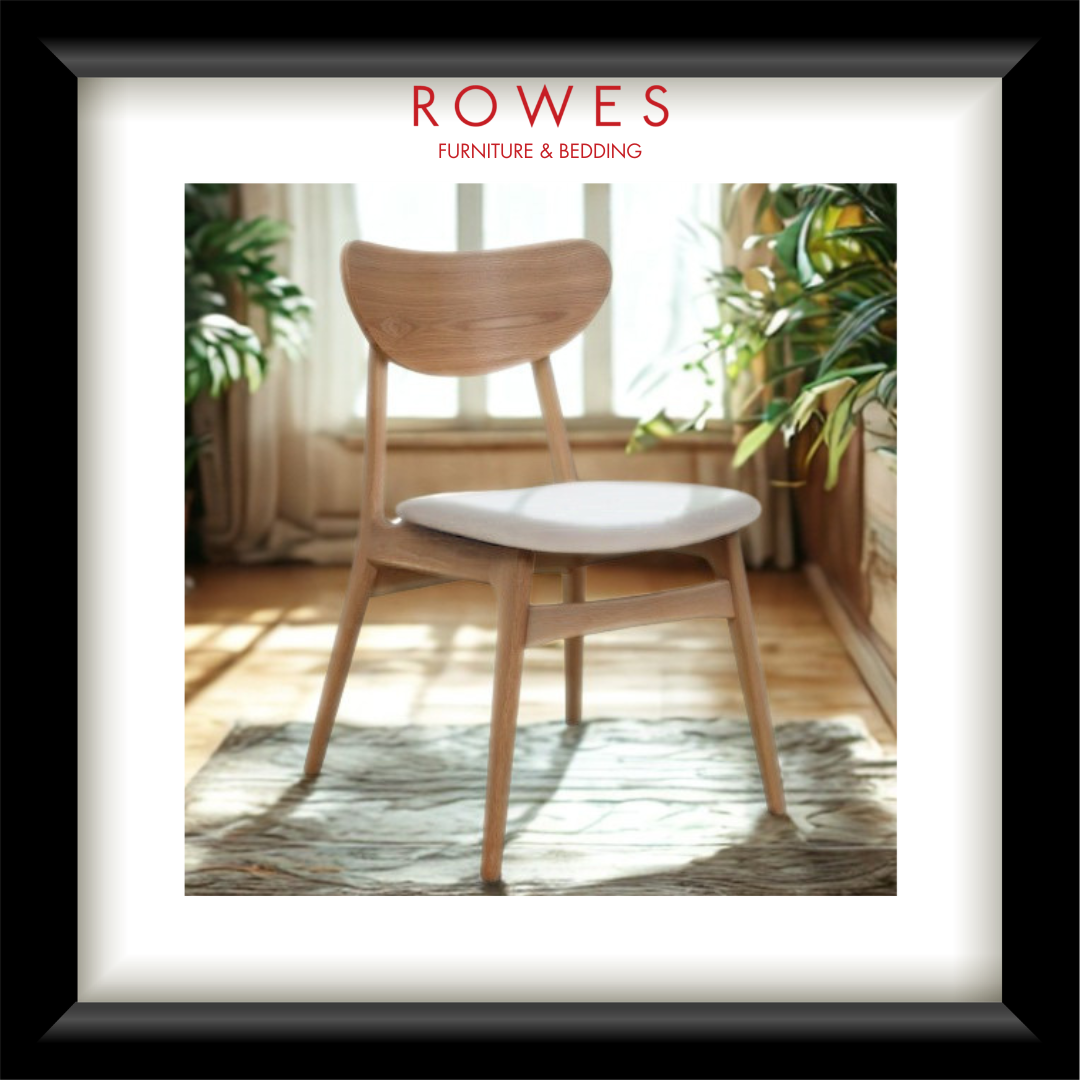 A framed interior photo print featuring a light wood dining chair with a white upholstered seat cushion in a sunlit room. The print has a white mat and a thick black frame, with the red text 'ROWES FURNITURE & BEDDOING' centered at the top.